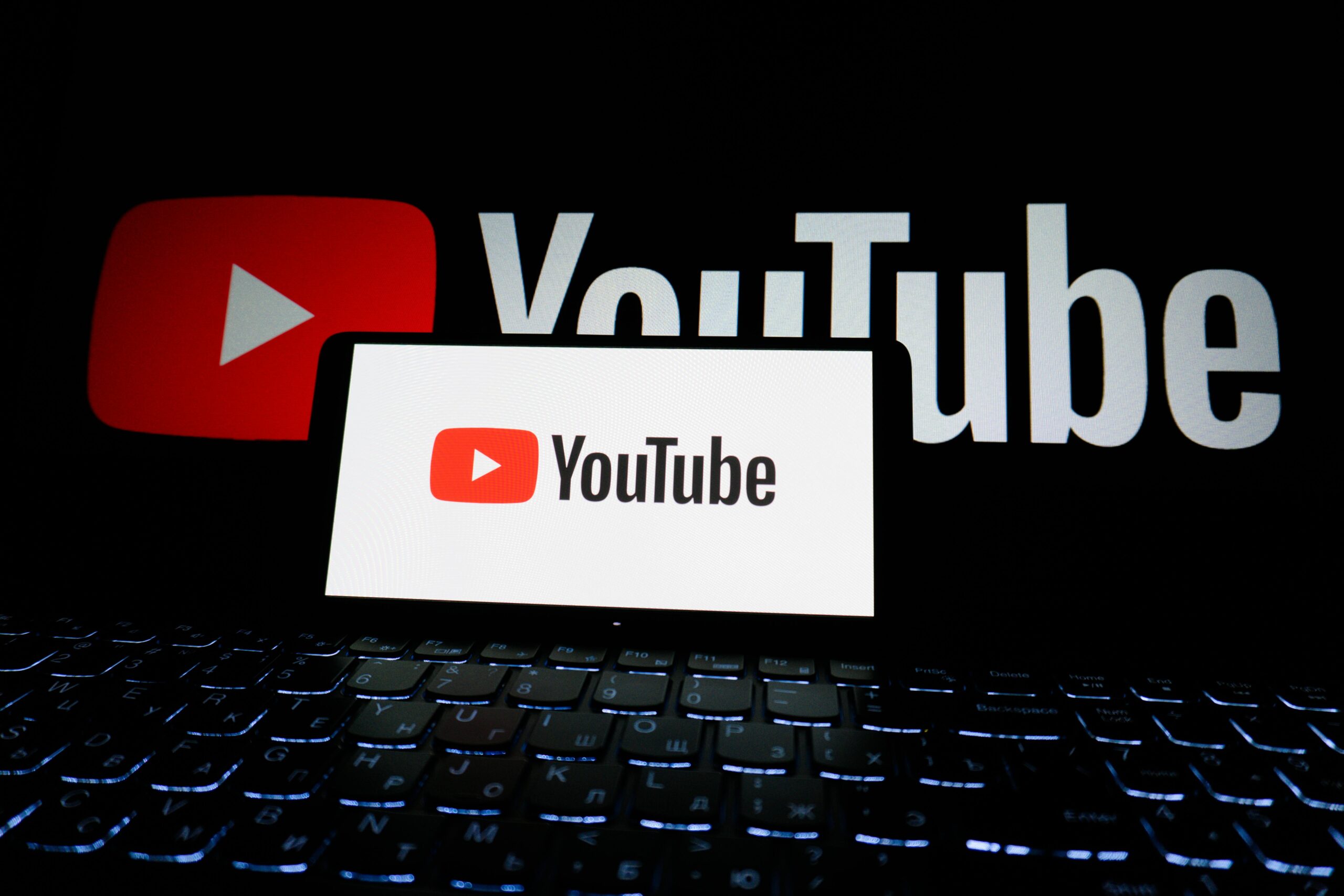 Close-up of YouTube logo displayed on a laptop screen in a dark environment.